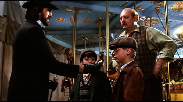 Carnival man in black offers a ticket to a boy beside a carousel as another boy and a shopkeeper watch - scene from a 1983 Disney film.